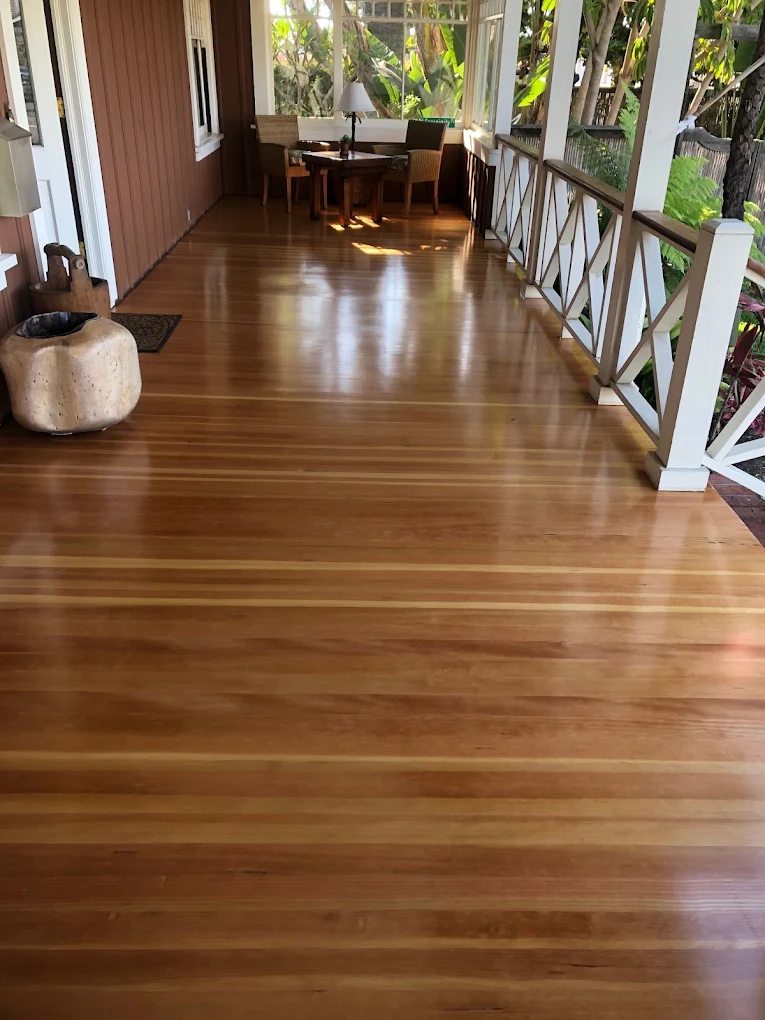 Glossy finished plank flooring on a covered porch, with white railings running down both sides.