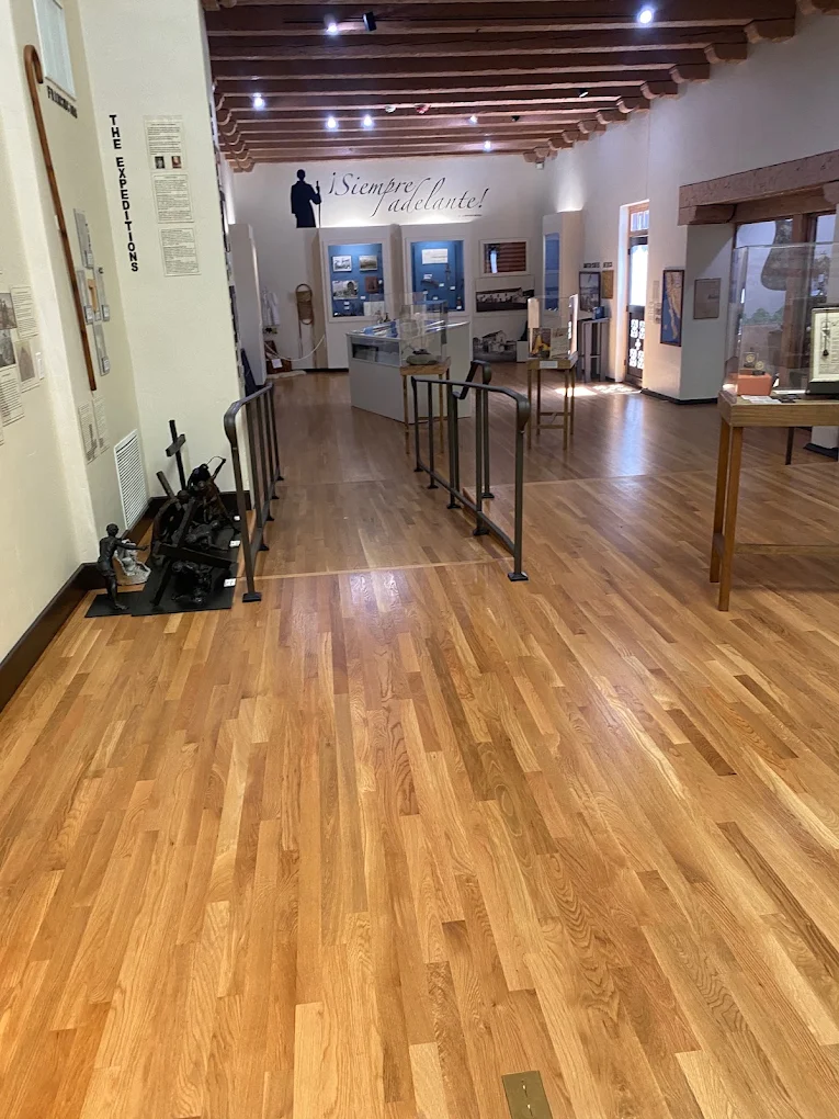 Narrow strip oak flooring running the length of a gallery hall with display cases and a wood beam ceiling.